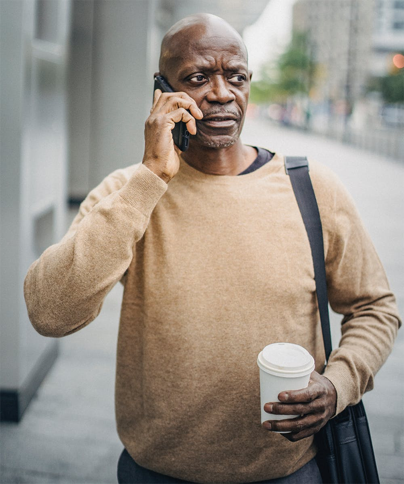 man in tan sweater talking on cell phone on city street